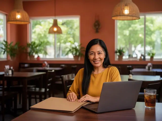 Smiling woman in a mustard blouse at a restaurant table with a kraft folder, laptop and iced tea
